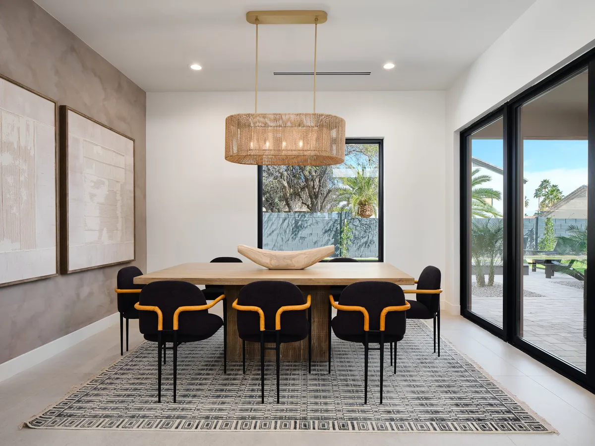 A sophisticated dining room featuring a large table with seating for eight, an elegant chandelier above, contemporary chairs, tasteful wall art, and plenty of natural light pouring in through the windows. The atmosphere is both formal and inviting, suited for celebratory feasts or intimate family dinners.