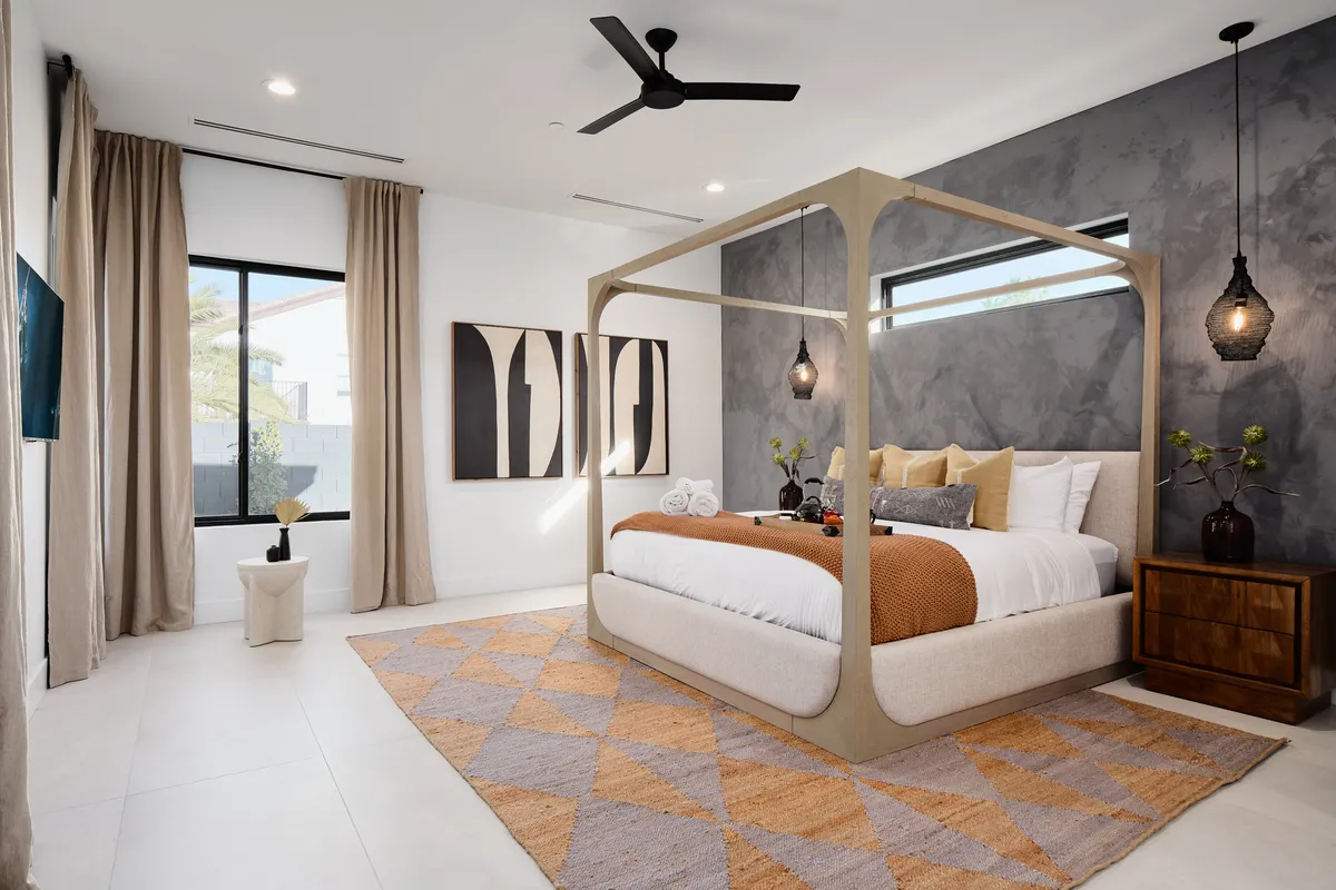 A tranquil bedroom featuring a four-poster bed dressed in designer bedding, soft area rug, decorative wall art, and a window allowing in natural light. The space is calm and refined, evoking a sense of peaceful retreat ideal for restful sleep.