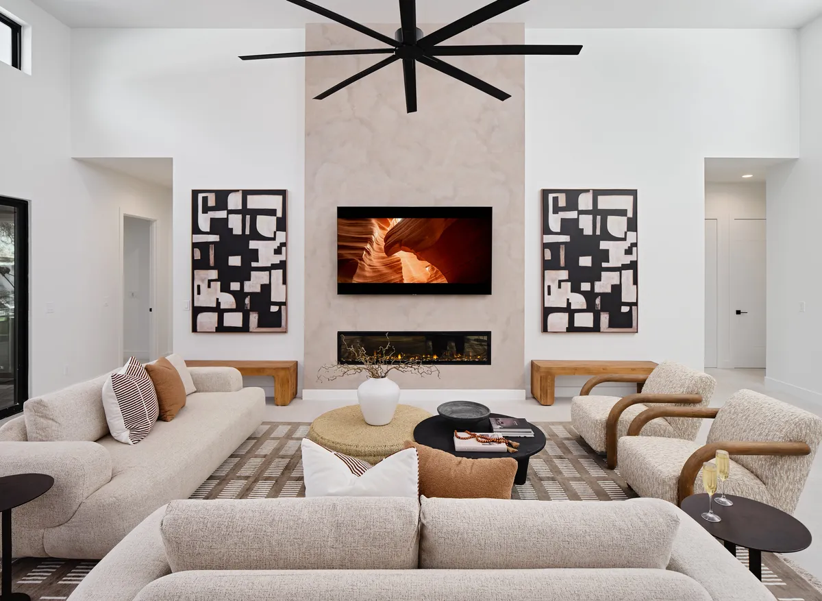 The image showcases a stylish, contemporary living room with a large wall-mounted television, a modern fireplace, chic art pieces, and a central coffee table. The space is designed for comfort and togetherness, inviting guests to gather for movie nights or cozy conversations.