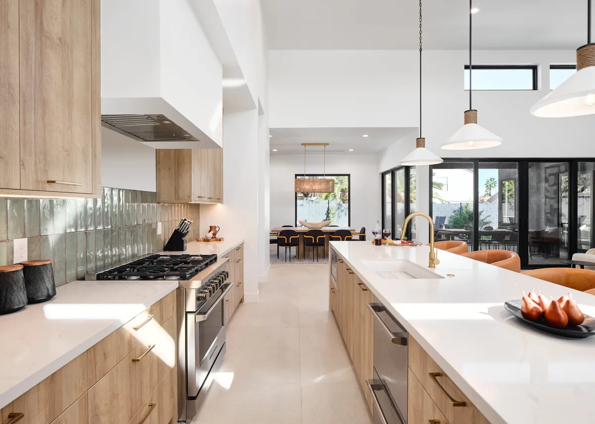 A warm and contemporary kitchen scene that captures the kitchen island, gleaming stainless steel appliances, a stylish backsplash, and a clear view into the connected dining area. The layout highlights seamless flow between the kitchen and dining space, underlining the home’s social and inviting character.
