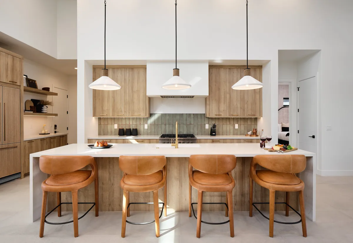 A bright, inviting kitchen featuring a spacious island with bar stools, elegant pendant lighting overhead, and sleek cabinetry lining the walls. The island is large enough for both meal preparation and casual gatherings, and the kitchen exudes a modern yet welcoming atmosphere—ideal for both everyday cooking and entertaining.