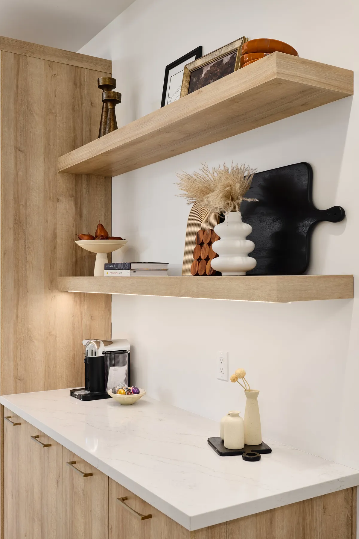A close-up view of a wooden shelving nook featuring a modern coffee machine, ceramic containers, and a decorative vase. The setup hints at a thoughtfully curated coffee bar area, inviting guests to brew a fresh cup in style and comfort.