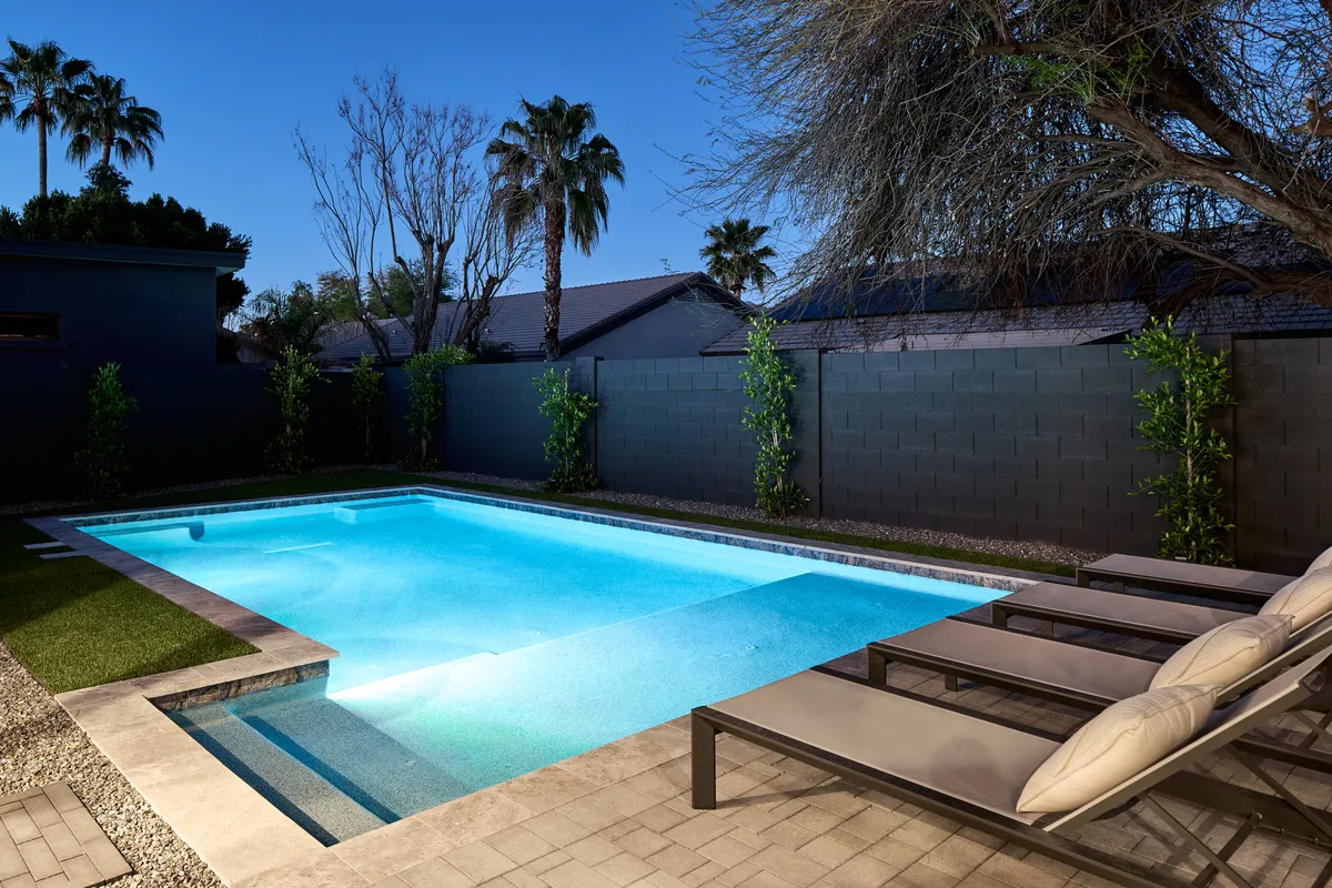 This serene exterior showcases a sparkling swimming pool surrounded by lounge chairs and palm trees, all within a private fenced area. The setting promises relaxation and group fun after a day at local events.