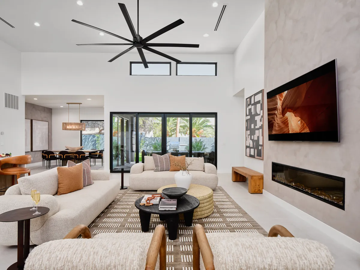 A contemporary interior featuring a comfortable seating arrangement with armchairs and a sofa, a modern fireplace set into the wall, and vibrant art pieces. Large windows allow radiant Southwest light to pour in, enhancing the welcoming mood and highlighting details such as natural textures and stylish decor.