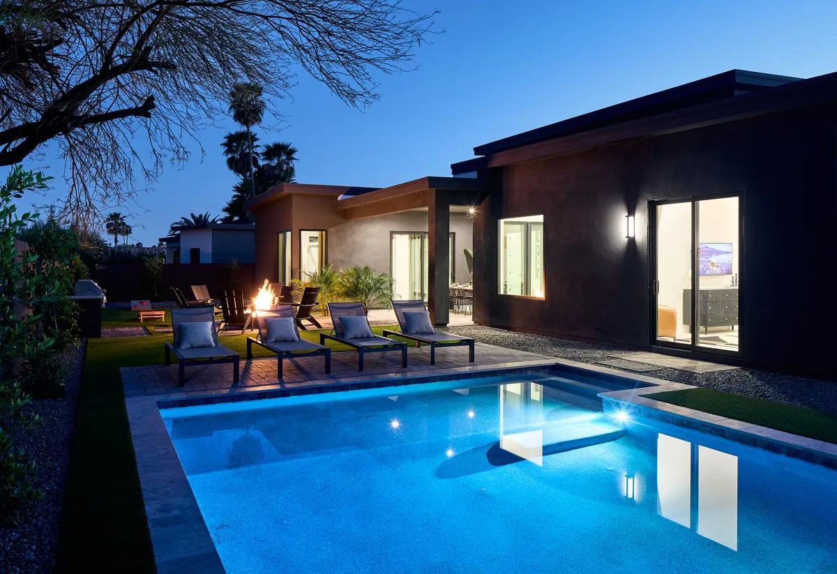 This image showcases a sparkling swimming pool surrounded by inviting lounge chairs, a modern house exterior, and a cozy fire pit area. The setting exudes relaxation and socialization, perfectly capturing the essence of the backyard sanctuary described in the section.