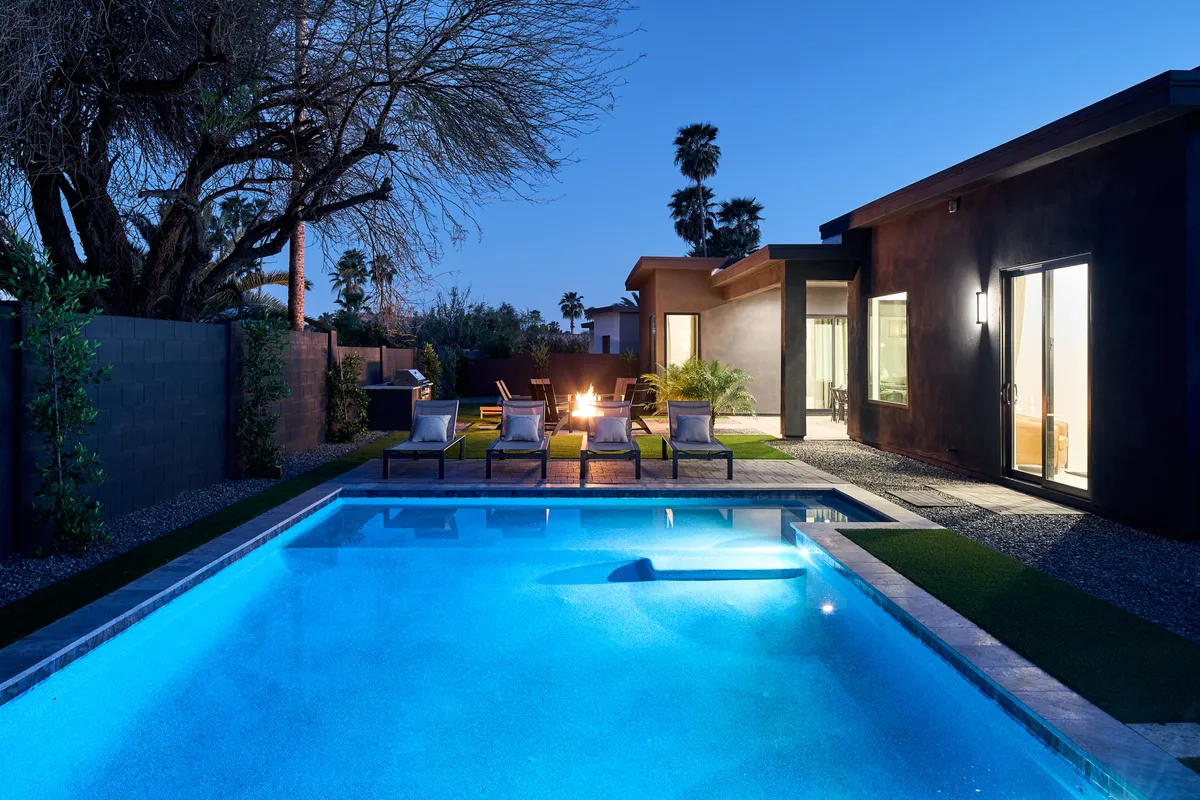 A striking exterior shot of Tulum House features a sparkling swimming pool surrounded by inviting lounge chairs and a cozy fire pit. The modern design of the house is accentuated by large windows that offer a glimpse of the stylish interiors.